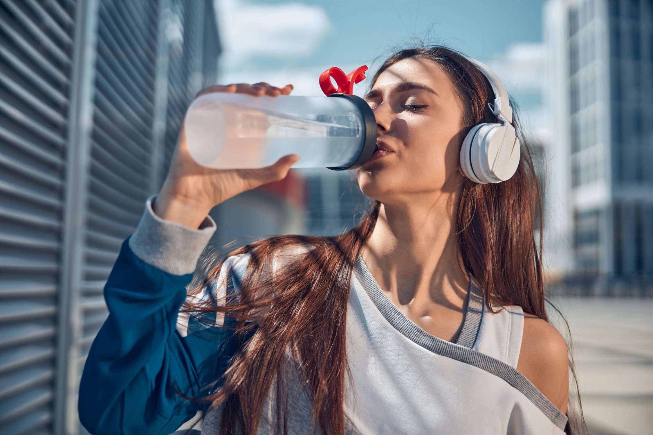 A Woman Wearing Headphones and Drinking Water